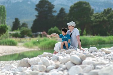 İnsan ve çocuk nehrin ya da gölün yanında oturuyorlar. Baba ve oğul. Babalar Günü.