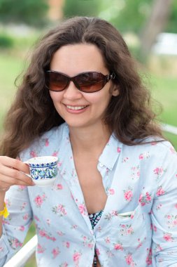 Elinde kahve fincanı olan kadın kumsalda oturuyor.