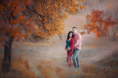 Kocasıyla sonbahar ormanında hamile bir kadın. Anne ve baba. Mutlu ebeveynler. Sonbahar aile portresi. Hamilelik, annelik, beklenti konsepti. Hamileliğin güzel ve hassas fotoğrafı..