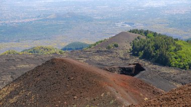 Etna Dağı volkanik kraterinin canlı kırmızı ve siyah lav kayalarıyla hava görüntüsü. Siyah volkanik kül, kırmızı renkli yamaçlar ve yeşil bitki örtüsü manzarası. Doğa, jeoloji ve Etna Dağı ile ilgili macera.