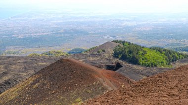 Etna Dağı volkanik kraterinin canlı kırmızı ve siyah lav kayalarıyla hava görüntüsü. Siyah volkanik kül, kırmızı renkli yamaçlar ve yeşil bitki örtüsü manzarası. Doğa, jeoloji ve Etna Dağı ile ilgili macera.