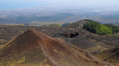 Etna Dağı volkanik kraterinin canlı kırmızı ve siyah lav kayalarıyla hava görüntüsü. Siyah volkanik kül, kırmızı renkli yamaçlar ve yeşil bitki örtüsü manzarası. Doğa, jeoloji ve Etna Dağı ile ilgili macera.