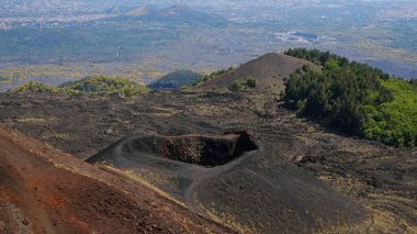 Etna Dağı volkanik kraterinin canlı kırmızı ve siyah lav kayalarıyla hava görüntüsü. Siyah volkanik kül, kırmızı renkli yamaçlar ve yeşil bitki örtüsü manzarası. Doğa, jeoloji ve Etna Dağı ile ilgili macera.