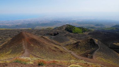 Etna Dağı volkanik kraterinin canlı kırmızı ve siyah lav kayalarıyla hava görüntüsü. Siyah volkanik kül, kırmızı renkli yamaçlar ve yeşil bitki örtüsü manzarası. Doğa, jeoloji ve Etna Dağı ile ilgili macera.