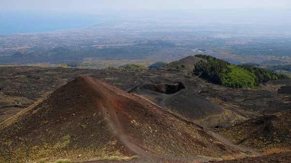 Etna Dağı volkanik kraterinin canlı kırmızı ve siyah lav kayalarıyla hava görüntüsü. Siyah volkanik kül, kırmızı renkli yamaçlar ve yeşil bitki örtüsü manzarası. Doğa, jeoloji ve Etna Dağı ile ilgili macera.