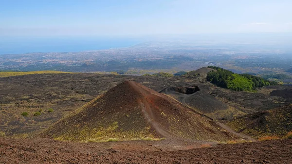 Etna Dağı volkanik kraterinin canlı kırmızı ve siyah lav kayalarıyla hava görüntüsü. Siyah volkanik kül, kırmızı renkli yamaçlar ve yeşil bitki örtüsü manzarası. Doğa, jeoloji ve Etna Dağı ile ilgili macera.