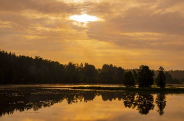 Suyun üzerinde sisli bir gölün üzerinde sabah güneşi doğuyor.