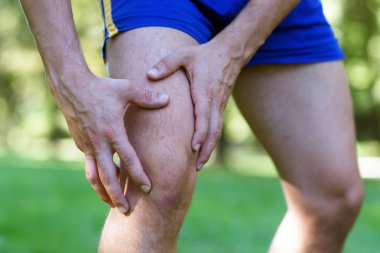 Parkta koşu çalışması sonrası diz yaralanması. Adam koşmayı bıraktı ve elini dizine dayadı. Gün ışığı ve sıcak etkisi ile Morning Shot.