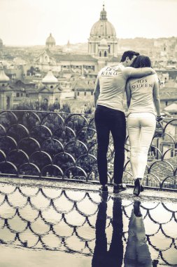 Roma, İtalya 'da tatilde kucaklaşan bir çift. Su birikintisindeki yansıma. Roma 'nın Pincio terası manzarası. Üzerinde Kral ve Kraliçe yazan tişört..