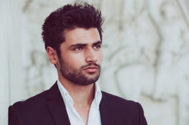 Güzel saçlı ve sakallı yakışıklı ve genç bir adam. Çekici bir adamın portresi. Beyaz gömlek ve ceket..