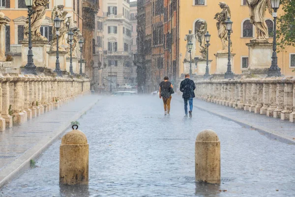 Rain in the historic center of Rome in Italy. Two people back to back walking under the storm. Sant Angelo bridge.