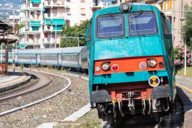 Tren raylarda, tren istasyonuna varmak üzere. Raylarda toplu taşıma. Kuzey İtalya 'da Liguria' da bir istasyonda. Gün zamanı.