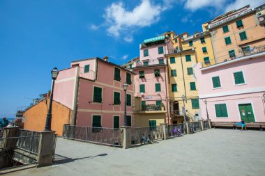 Riomaggiore, İtalya. 15 Ağustos 2020: İtalya 'nın Riomaggiore şehrinde renkli evler manzaralı meydan. Mavi gökyüzü, bazı insanlar var.