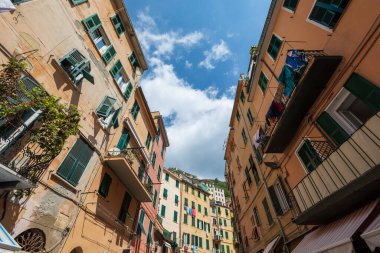 Riomaggiore, İtalya. 15 Ağustos 2020: İtalya 'nın Riomaggiore kentindeki renkli evlerin perspektif manzarası. Mavi gökyüzü. Balkonlu ve pencereli saraylar.