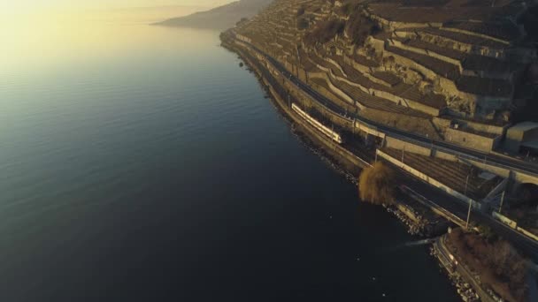 Der Zug fährt bei Sonnenuntergang am Genfer See entlang. Weinberge von Lavaux. Luftbild — Stockvideo