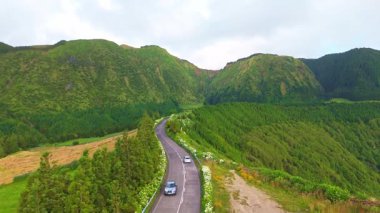 Ortancalarla Yoldaki Araba. Yeşil Tarlalar, Orman ve Tepeler. Azores, Sao Miguel Adası. Portekiz. Hava görüntüsü. Drone İleri ve Yukarı Gidiyor