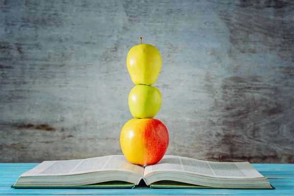 Open boek en appels gestapeld voor houten achtergrond — Stockfoto