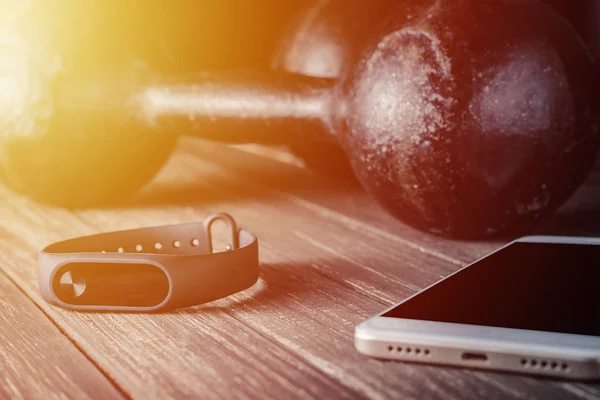 fitness tracker, smartphone and dumbbells on wooden background