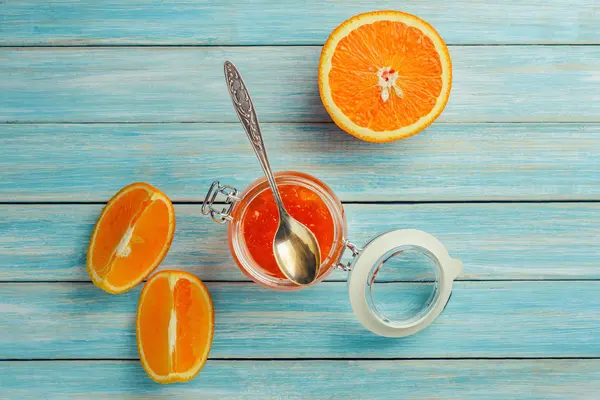 Compota de laranja em frasco de vidro e pedaços de laranja no fundo de madeira azul — Fotografia de Stock