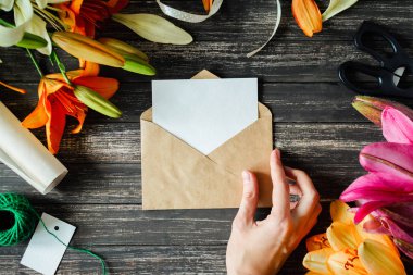 Mockup beyaz tebrik kartı ve koyu ahşap arka plan üzerinde lilyum çiçeklerle zanaat zarf