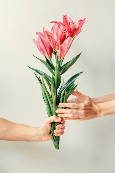 Man\'s hand giving bouquet of lilies flowers to woma\'s hand