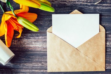 Mockup beyaz tebrik kartı ve ahşap arka plan üzerinde lilyum çiçeklerle zanaat zarf