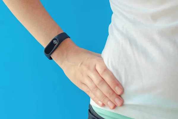 Young woman with fitness tracker on hand on blue background — Stock Photo, Image