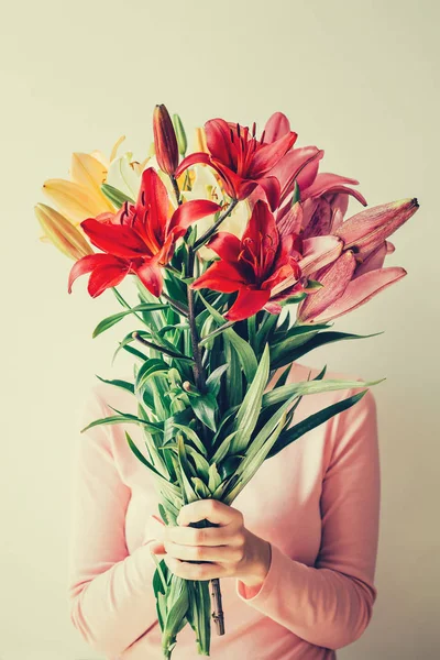 Девушка держит букет лилий в руках, прячет лицо в цветах — стоковое фото