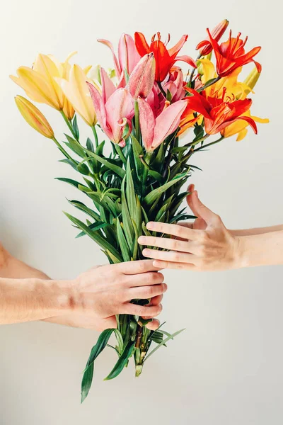 Man\'s hand giving bouquet of flowers to woma\'s hand on white background