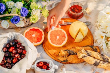 Parkta piknik gün batımında. Meyve, peynir masa örtüsü üstten görünüm üzerinde bir ay çöreği. Kadın eli meyve alır