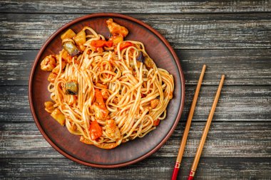 Udon erişte ile tavuk, tatlı tavada ve sos ve yemek çubukları üzerinde ahşap masa ekşi
