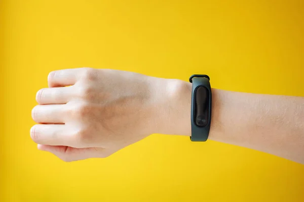 Woman's hand with fitness tracker on yellow background