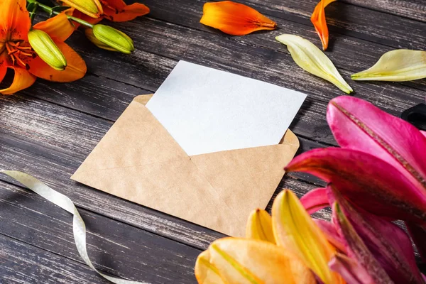 Sábana blanca en blanco en sobre kraft y flores sobre fondo de madera oscura — Foto de Stock