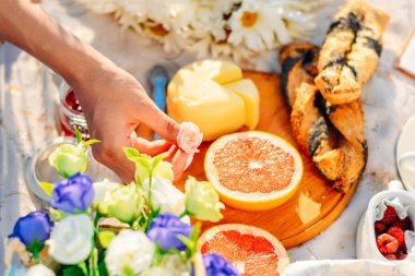 Gün batımında piknik. Meyve, peynir bir kruvasan masa örtüsü üzerinde. kadın eli tutun pembe gül