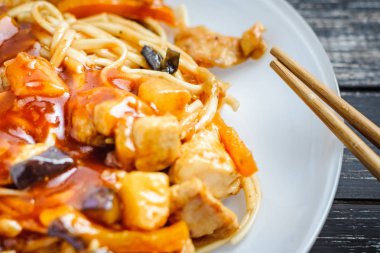 Çin noodle udon, ekşi-tatlı soslu tavuk ve ahşap masa üzerinde yemek çubukları ile. Asya Wok gıda
