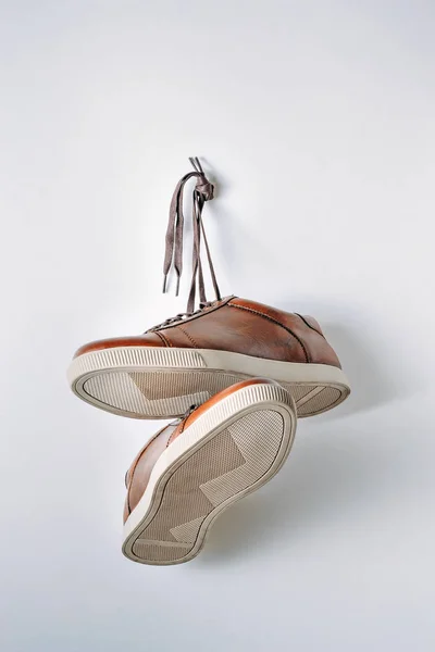 Zbliżenie na brązowe skórzane męskie buty powiesić na paznokciu na białym tle — Zdjęcie stockowe