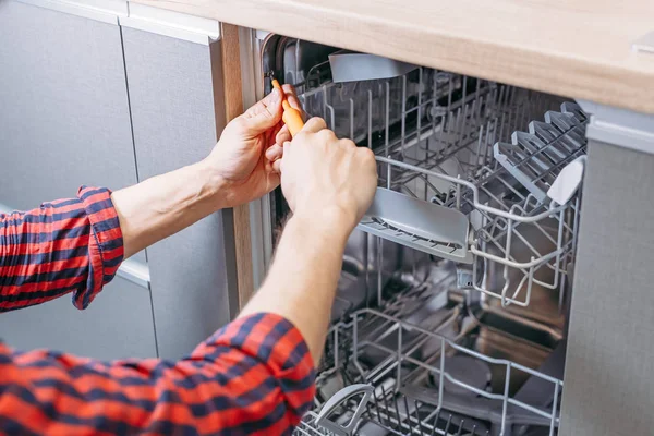 Man reparera diskmaskin. Manlig hand med skruvmejsel installerar vitvaror — Stockfoto