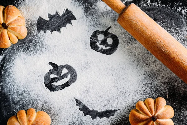 Drawing Halloween pumpkin head jack lantern and bat on wheat flour background with cakes in the shape of pumpkin, top view