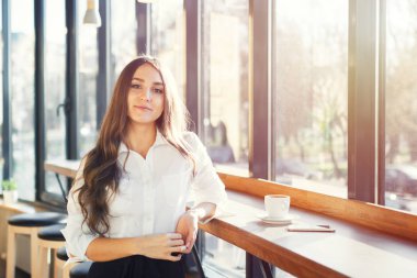 Güzel genç kadın beyaz bluz kahve içmek ve kafede smartphone kullanarak