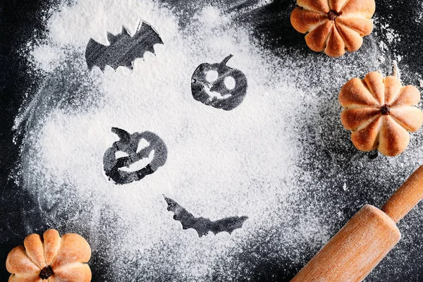 Drawing Halloween decorations on flour background, cakes in the shape of pumpkin and rolling pin. Halloween cooking concept