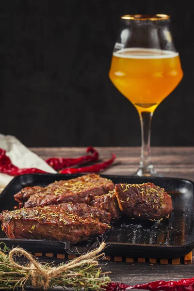 Жареные мясные стейки на сковороде и стакан пива на темном деревянном фоне — стоковое фото
