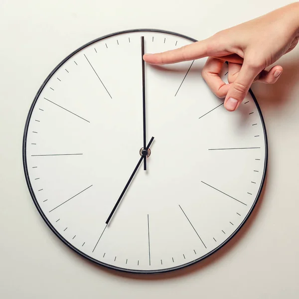 Woman hand stop time on a round clock, female finger takes the minute arrow of the clock back, time management and deadline concept