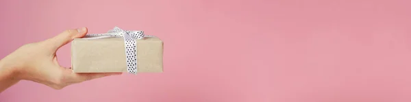 Main de femme tient boîte cadeau sur fond rose, bannière avec espace de copie — Photo
