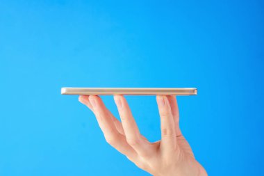 Kadın el smartphone mavi arka plan üzerinde tutar.