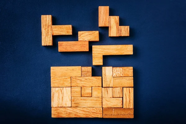 Různé geometrické tvary dřevěných bloků uspořádat v solidní obrázek na tmavém pozadí. Kreativní a logické myšlení a koncepce řešení problémů — Stock fotografie