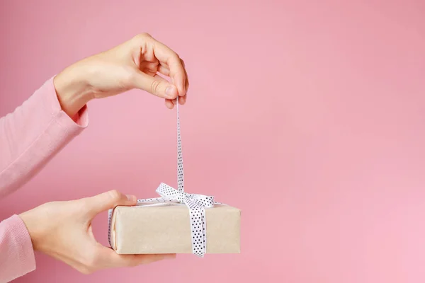 Donna mani sciogliere fiocco su scatola regalo su uno sfondo rosa — Foto Stock