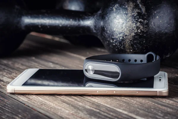 fitness tracker, smartphone and iron dumbbells on a wooden background