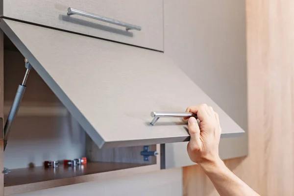Мужчина вручную открывает кухонный шкаф с ручкой — стоковое фото