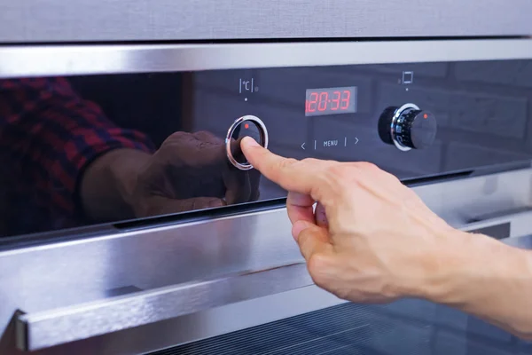 Чоловік встановлює режим приготування їжі на електричній печі. Натисніть кнопку чоловічого пальця на панелі керування на піч, крупним планом — стокове фото