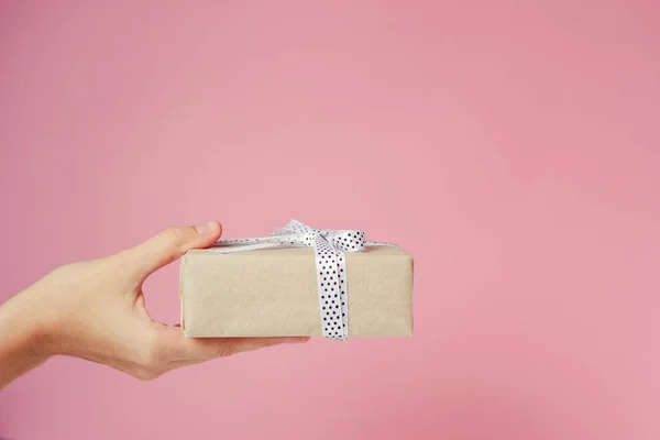 La mano della donna tiene la scatola regalo su sfondo rosa con spazio di copia — Foto Stock